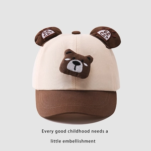 Dettaglio cappellino neonato con orecchie d'orso 3D e ricamo cartoon su tessuto beige
