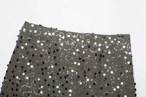 Dettaglio macro di paillettes a onde argento e nere su tessuto di base verde oliva