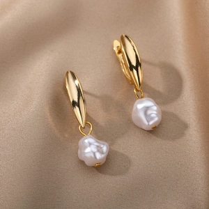 Detailed close-up of golden leaf-shaped clasp and white baroque pearl earrings on silk