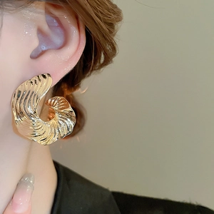 Close-up of model wearing large golden wavy textured earrings in a minimalist style