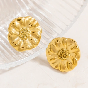 Macro shot of gold floral stud earrings with metallic texture on striped glass surface