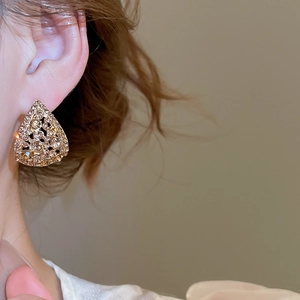 Close-up of golden hollow triangle earrings with sparkling crystals worn by a model