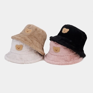 Detail view of four plush bucket hats with bear patches in cream, khaki, pink, and black