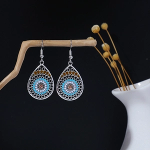 Detail of ethnic silver teardrop earrings with blue floral patterns and amber zircon