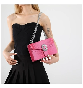 Detail of pink croc-embossed crossbody bag featuring crystal buckle and silver chain