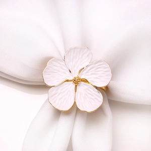 Elegant gold-plated napkin ring with a white floral motif on a white fabric napkin