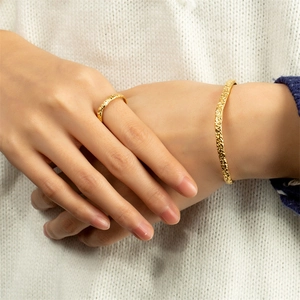 Close-up of golden hammered texture ring and slim open cuff bracelet on model