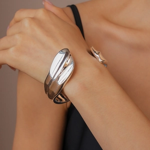 Close-up of a wide silver fluid-style open cuff bracelet with glossy metallic texture