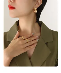 Close-up of golden fan-shaped textured earrings and rings on a model in a green suit