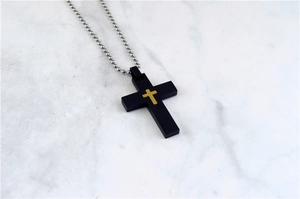 Close-up of punk style black and gold cross pendant on a silver ball chain necklace