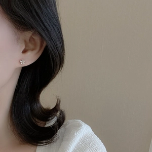 Minimalist silver flower stud earrings with zircon stones worn by a model in soft light