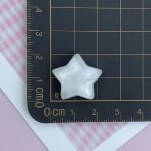 Detailed view of a 2.5cm white glitter star resin accessory on a black measuring mat