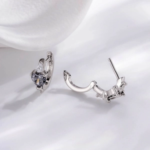 Silver heart-shaped earrings with grey zircon stones on soft white silk background