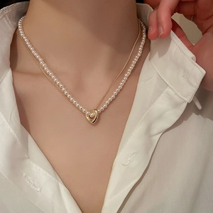 Detail view of layered pearl necklace with golden heart pendant on white shirt