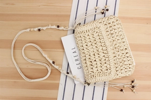 Detail of woven straw shoulder bag featuring decorative wooden beads and fringe tassels