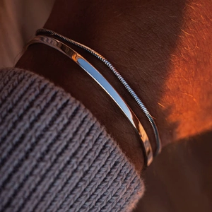 Détail d'un ensemble de bracelets argentés pour hommes sur un poignet avec manche tricotée