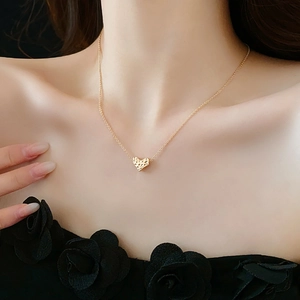 Detail of a gold heart pendant necklace on model with hammered metal texture and gold finish