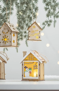 Dettaglio di una casetta di Natale in legno con LED appesa a un ramo di pino