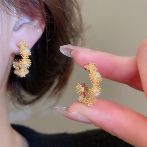 Detailed close-up of C-shaped flower earrings with gold plating and zircon stones