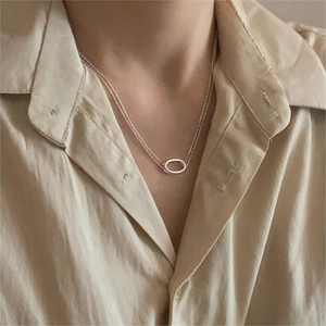 Close-up of minimalist silver layered necklace with oval pendant on a model wearing linen