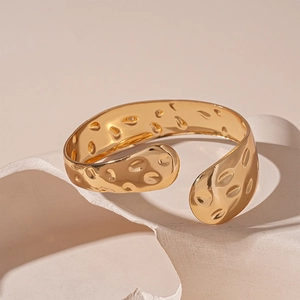 Dettaglio di un bracciale rigido dorato geometrico con moderna texture martellata