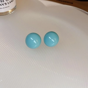 Detailed macro view of bright blue spherical stud earrings on a textured white tray