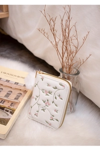 Detail of white embroidered flower wallet with gold zipper and soft pompom charm