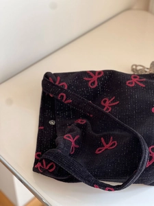 Detail of black tweed shoulder bag with red bow embroidery and shimmering silver threads