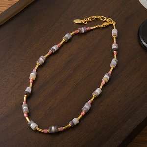 Collana boho in pietra naturale con tubi dorati su un vassoio in legno vintage