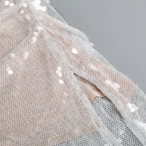 Makroaufnahme von silbernen Pailletten auf weißem Netzstoff für ein elegantes Abendkleid