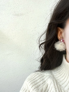Close-up of red plaid fabric stud earrings with cream pom-poms worn by a model