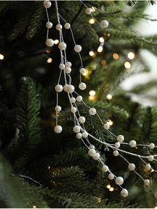 Close-up of white decorative pearl garland on Christmas tree with warm bokeh background