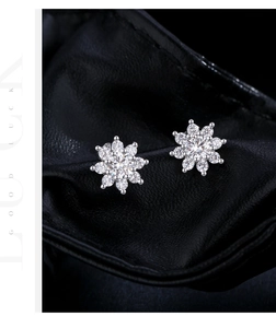 Macro shot of silver flower earrings with crystals on a textured black surface