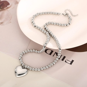 Detail of silver stainless steel bead necklace with heart pendant on a pink tray