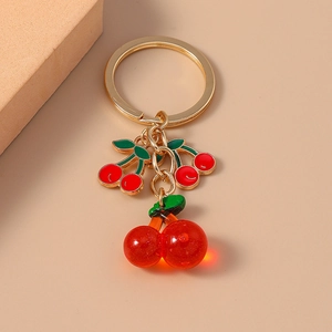 Golden cherry keychain with red resin fruit and enamel charms on a beige background
