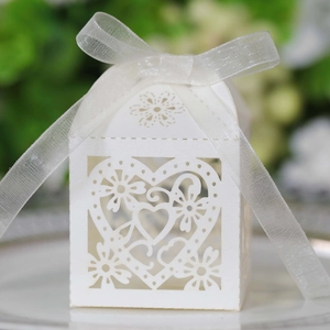 Detail of white laser-cut wedding favor box with heart patterns and organza ribbon
