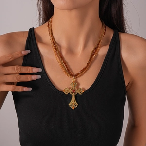 Detail of vintage multilayer beaded necklace with golden cross pendant and red gemstone