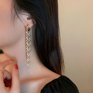 Detail eines langen Goldquastenohrrings mit Perlen und Metallperlen am Modell