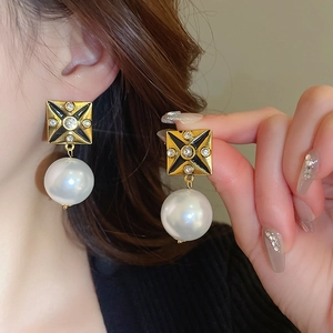 Detail of vintage square gold earrings with black enamel star and large white pearl