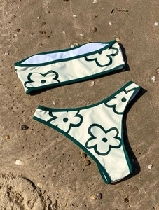 Detailed flat lay of cream floral bikini set on sunny beach sand with natural shells