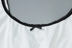 Vue détaillée de l'encolure blanche avec bordure en dentelle noire et petit nœud