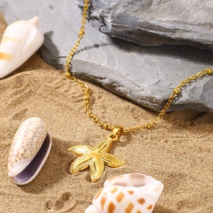 Golden starfish pendant necklace on beach sand with shells showing summer vacation vibes