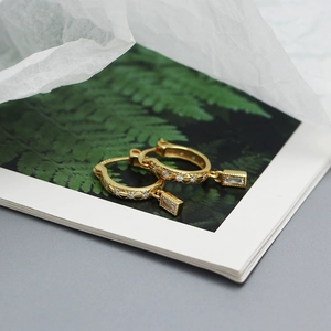 Close-up of gold starburst hoop earrings with a rectangular clear crystal drop pendant