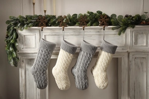 Detail of four cable knit Christmas stockings in grey and ivory hanging on a white mantel