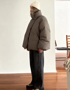 Close-up of a brownish-grey oversized padded jacket with a white beanie on a model