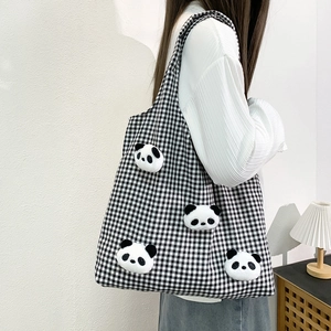 Close-up of a black and white checkered canvas tote bag with 3D plush panda dolls decoration