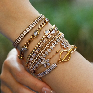 Close-up of a stacked gold bracelet set with heart charms and zircon on a woman's wrist