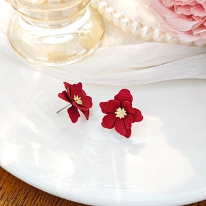 Close-up of red flower stud earrings with gold stamen detail on a white ceramic plate