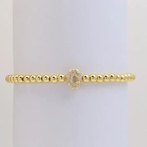 Close-up of golden beaded elastic bracelet featuring a sparkling zircon initial C charm
