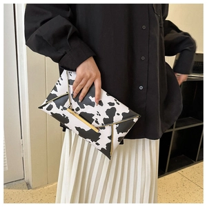 Detail of cow print envelope clutch featuring golden metal buckle and metallic trim
